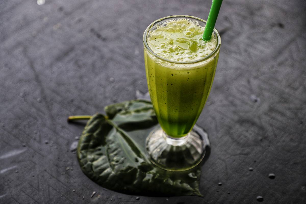 nutritional blend organic smoothy super green showing vibrant green smoothie in glass jar with visible spinach, cucumber, avocado, and lemon wedge beside it